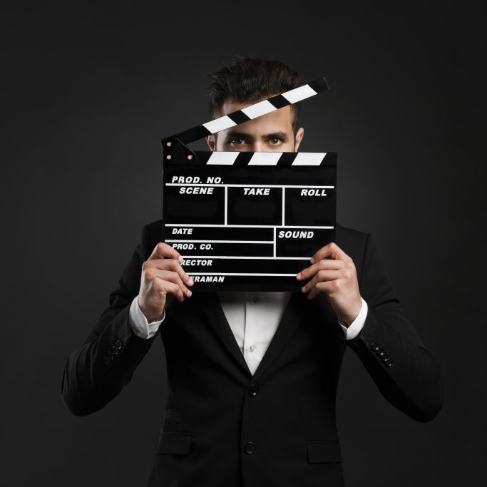 Handsome young man wearing a tuxedo and holding a clapboard